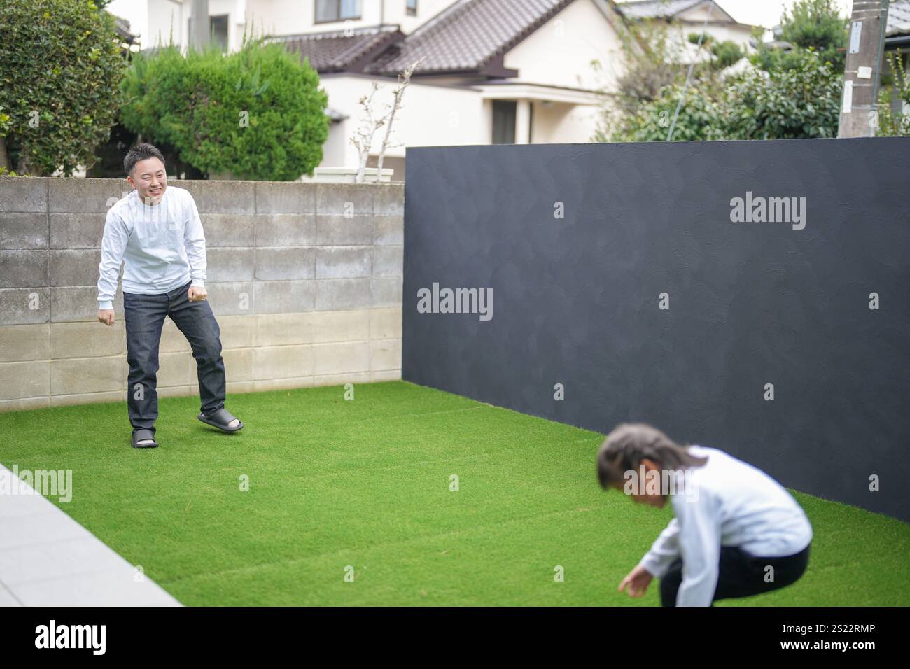 Un parent japonais et un enfant, un homme dans la vingtaine et une fille de 6 ans, jouent en se jetant des balles en plastique vert l'un sur l'autre dans le jardin clôturé de Banque D'Images