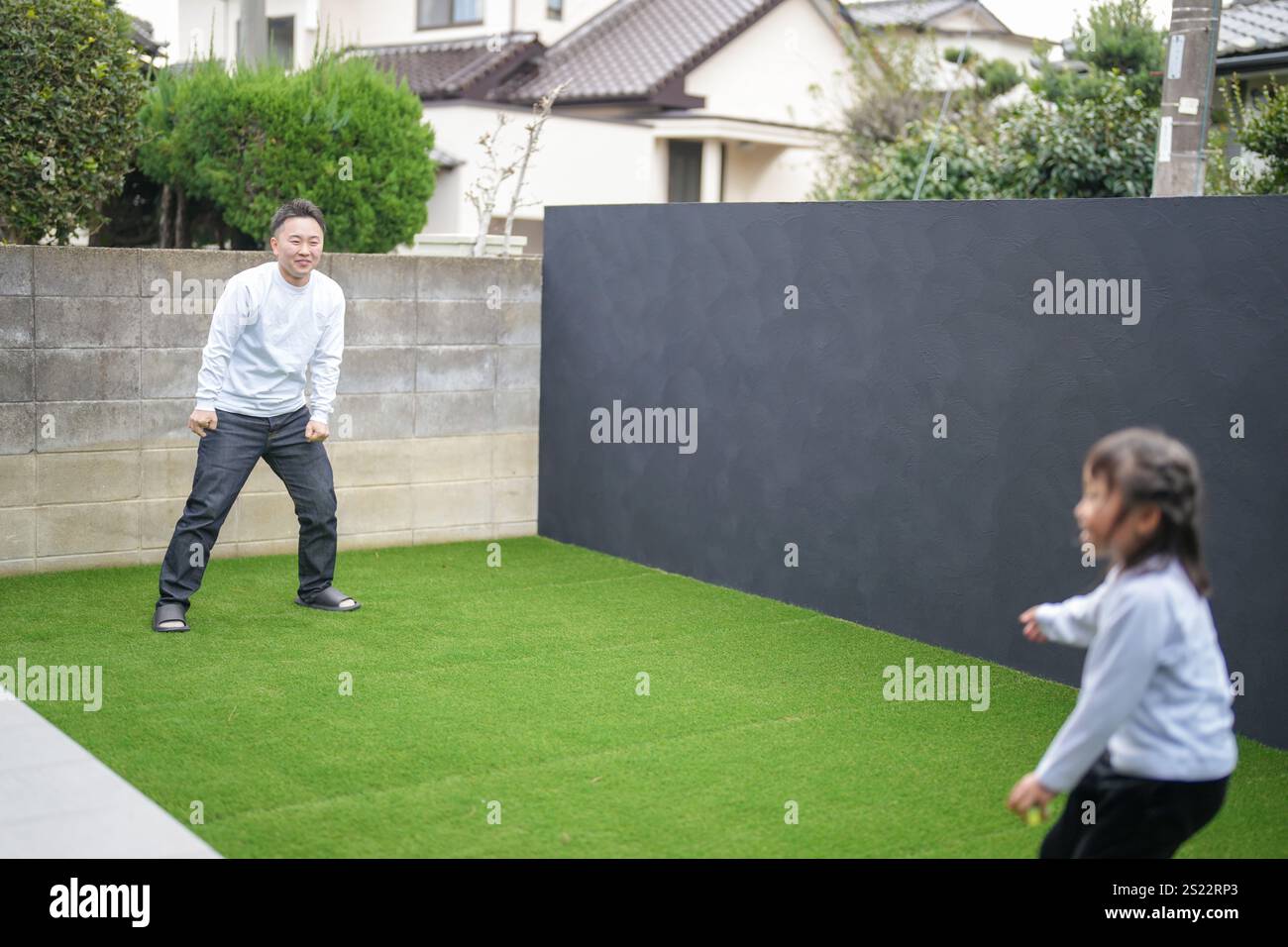 Un parent japonais et un enfant, un homme dans la vingtaine et une fille de 6 ans, jouent en se jetant des balles en plastique vert l'un sur l'autre dans le jardin clôturé de Banque D'Images