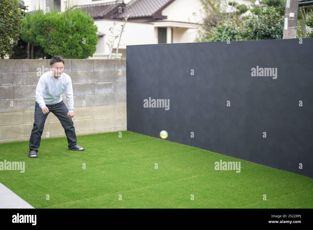 Un parent japonais et un enfant, un homme dans la vingtaine et une fille de 6 ans, jouent en se jetant des balles en plastique vert l'un sur l'autre dans le jardin clôturé de Banque D'Images