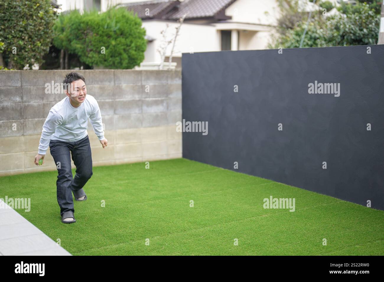Un parent japonais et un enfant, un homme dans la vingtaine et une fille de 6 ans, jouent en se jetant des balles en plastique vert l'un sur l'autre dans le jardin clôturé de Banque D'Images