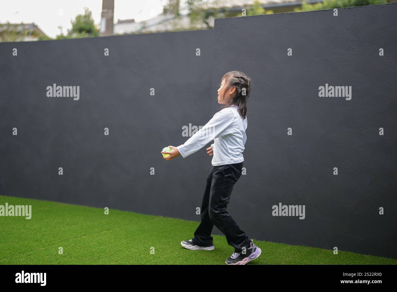 Un parent japonais et un enfant, un homme dans la vingtaine et une fille de 6 ans, jouent en se jetant des balles en plastique vert l'un sur l'autre dans le jardin clôturé de Banque D'Images