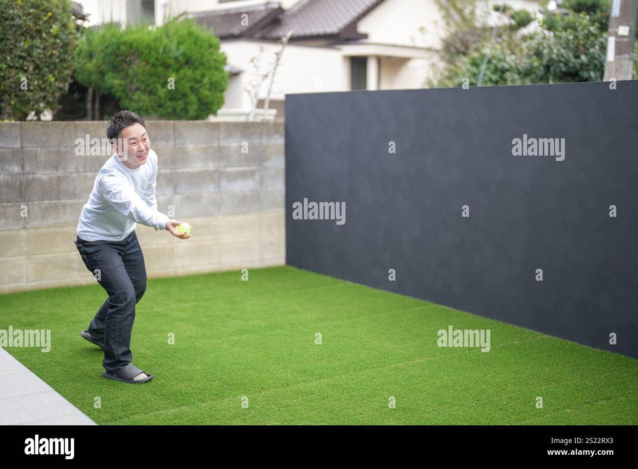 Un parent japonais et un enfant, un homme dans la vingtaine et une fille de 6 ans, jouent en se jetant des balles en plastique vert l'un sur l'autre dans le jardin clôturé de Banque D'Images