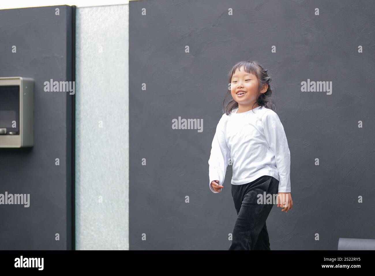 Un parent japonais et un enfant, un homme dans la vingtaine et une fille de 6 ans, jouent en se jetant des balles en plastique vert l'un sur l'autre dans le jardin clôturé de Banque D'Images