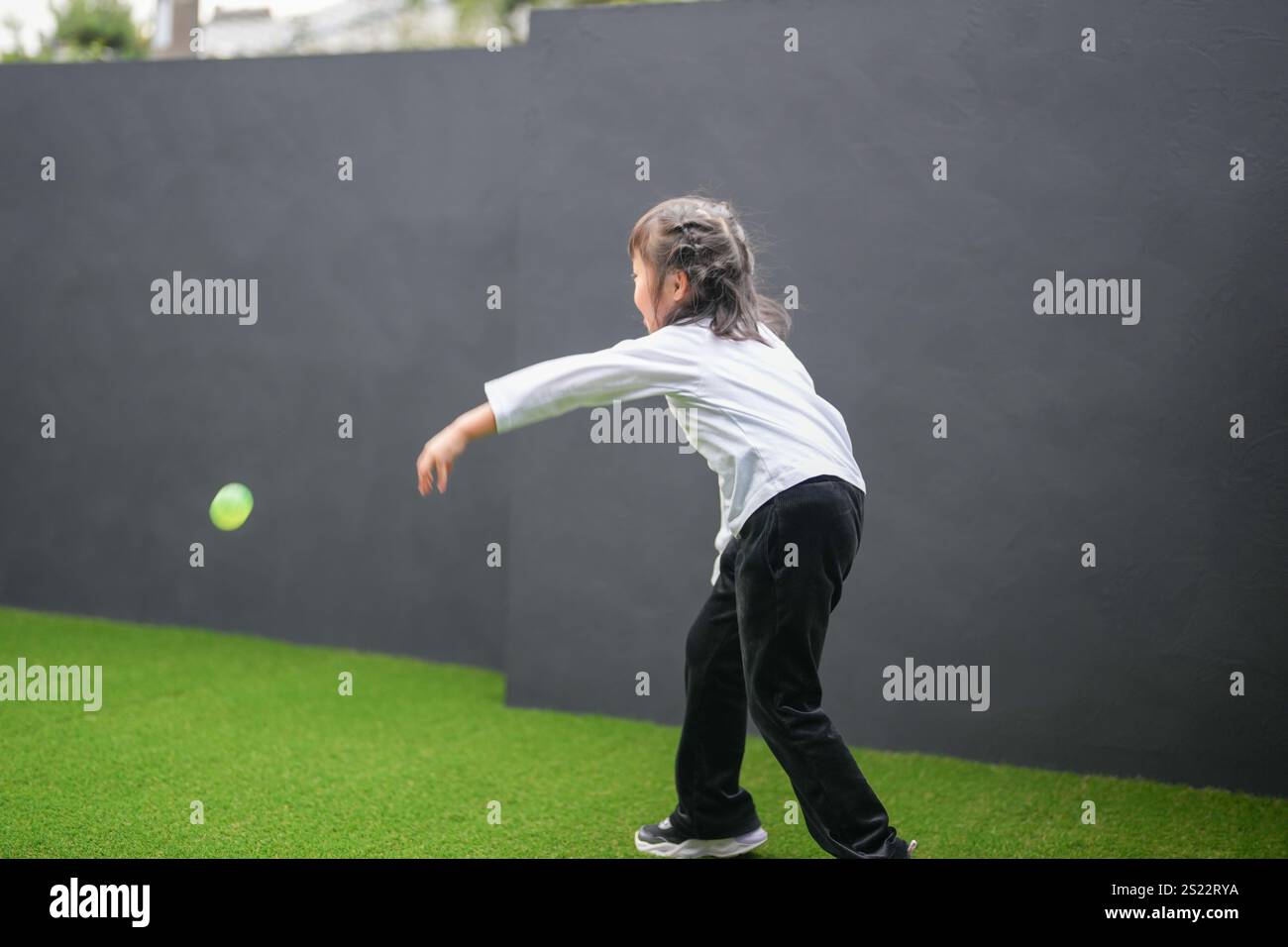 Un parent japonais et un enfant, un homme dans la vingtaine et une fille de 6 ans, jouent en se jetant des balles en plastique vert l'un sur l'autre dans le jardin clôturé de Banque D'Images