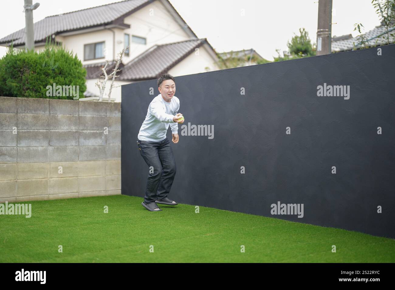 Un parent japonais et un enfant, un homme dans la vingtaine et une fille de 6 ans, jouent en se jetant des balles en plastique vert l'un sur l'autre dans le jardin clôturé de Banque D'Images