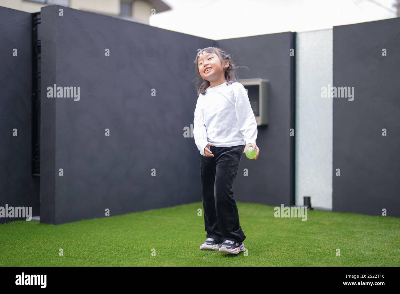 Un parent japonais et un enfant, un homme dans la vingtaine et une fille de 6 ans, jouent en se jetant des balles en plastique vert l'un sur l'autre dans le jardin clôturé de Banque D'Images