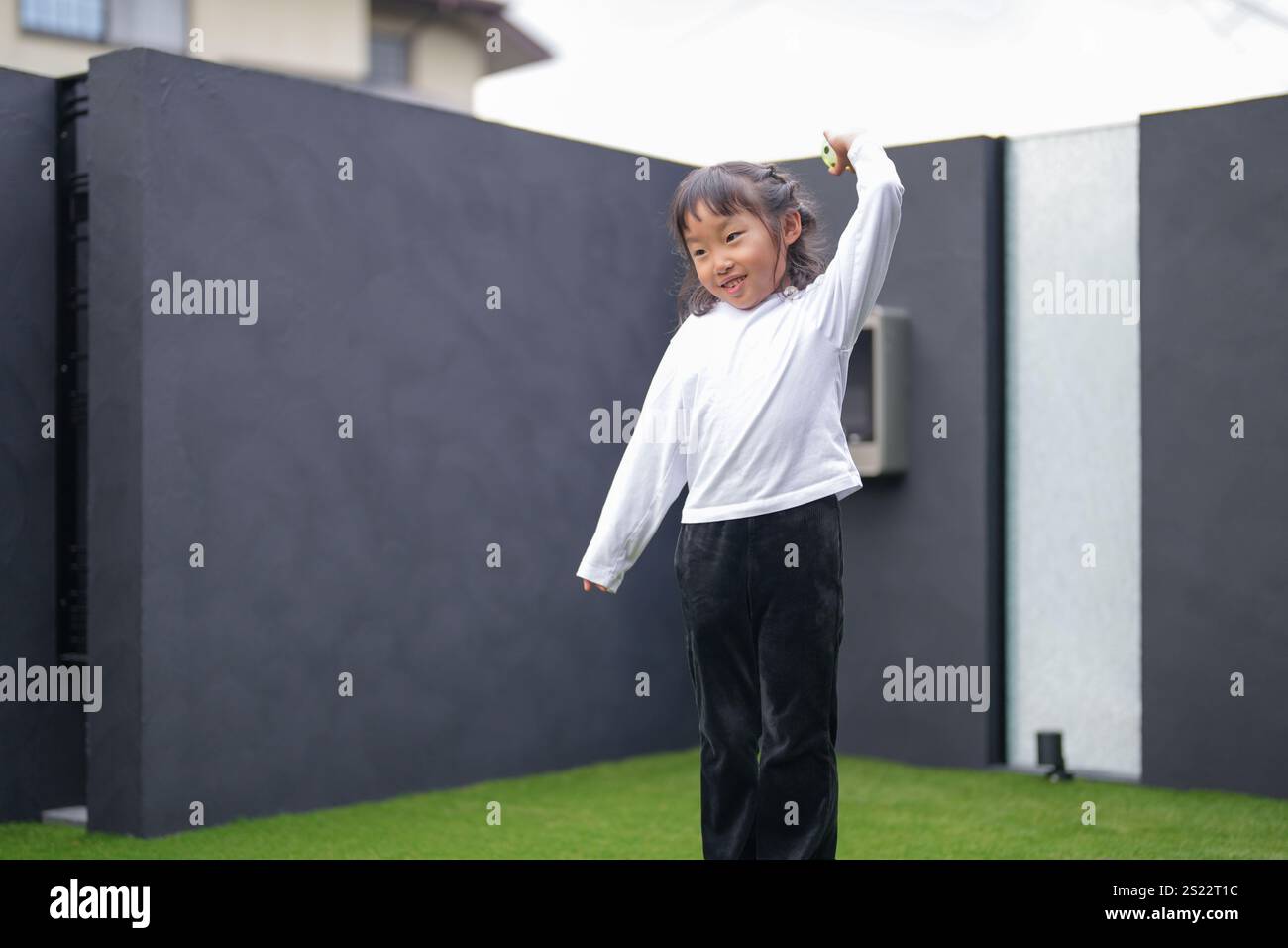 Un parent japonais et un enfant, un homme dans la vingtaine et une fille de 6 ans, jouent en se jetant des balles en plastique vert l'un sur l'autre dans le jardin clôturé de Banque D'Images