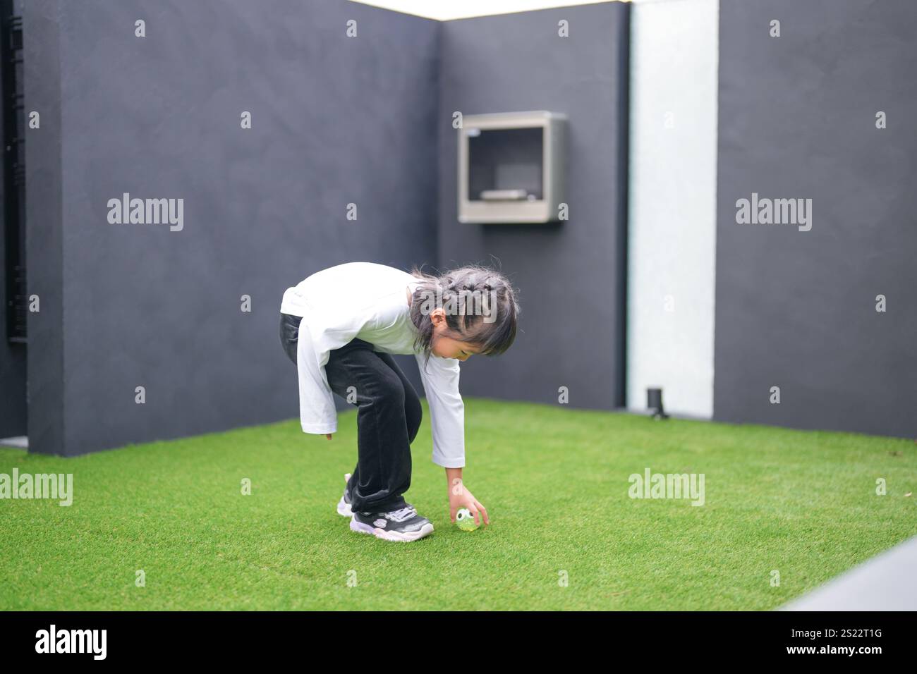 Un parent japonais et un enfant, un homme dans la vingtaine et une fille de 6 ans, jouent en se jetant des balles en plastique vert l'un sur l'autre dans le jardin clôturé de Banque D'Images