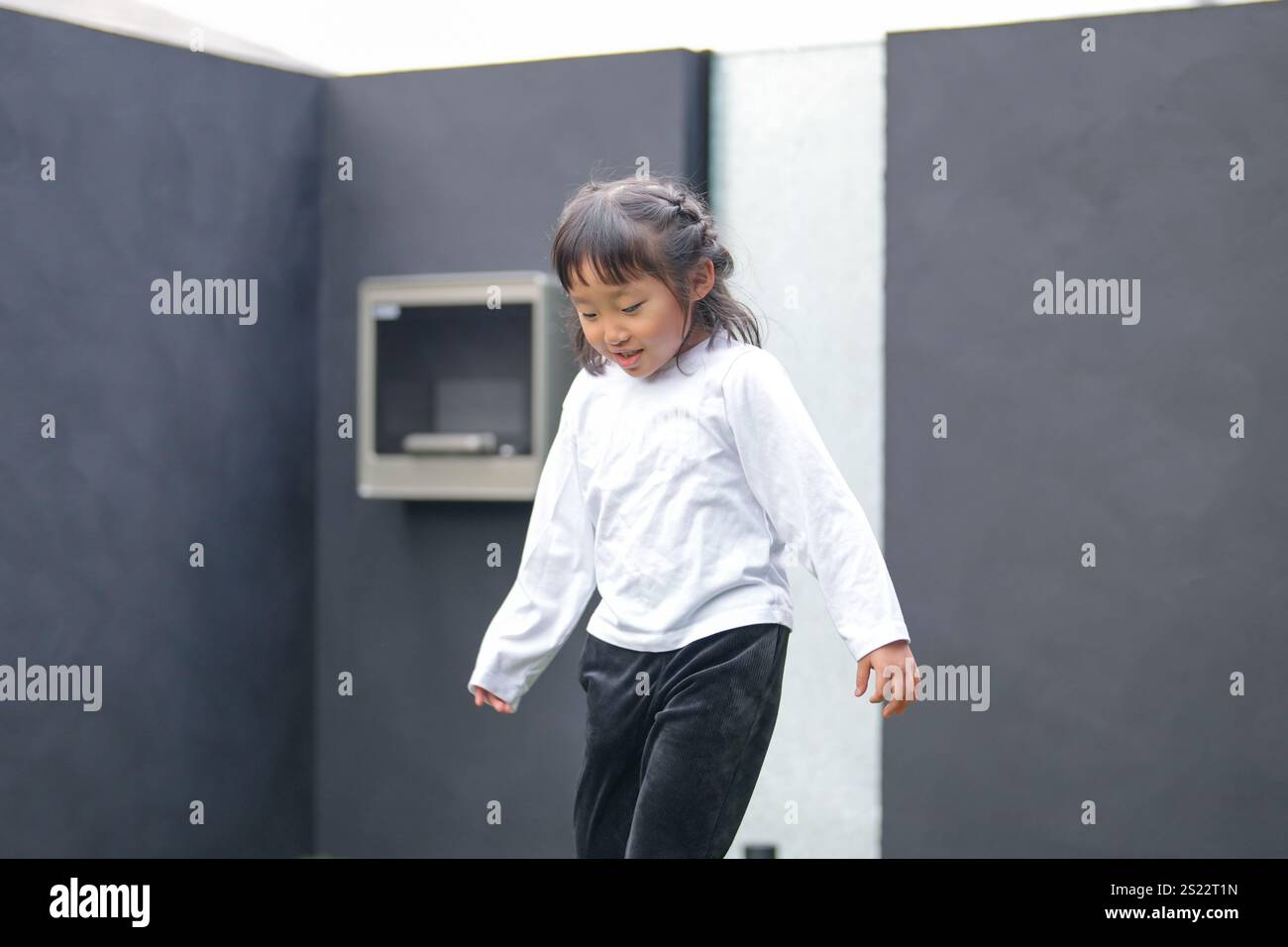 Un parent japonais et un enfant, un homme dans la vingtaine et une fille de 6 ans, jouent en se jetant des balles en plastique vert l'un sur l'autre dans le jardin clôturé de Banque D'Images