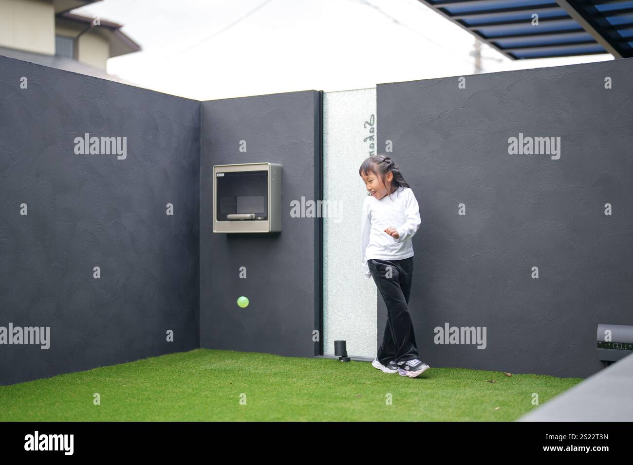 Un parent japonais et un enfant, un homme dans la vingtaine et une fille de 6 ans, jouent en se jetant des balles en plastique vert l'un sur l'autre dans le jardin clôturé de Banque D'Images