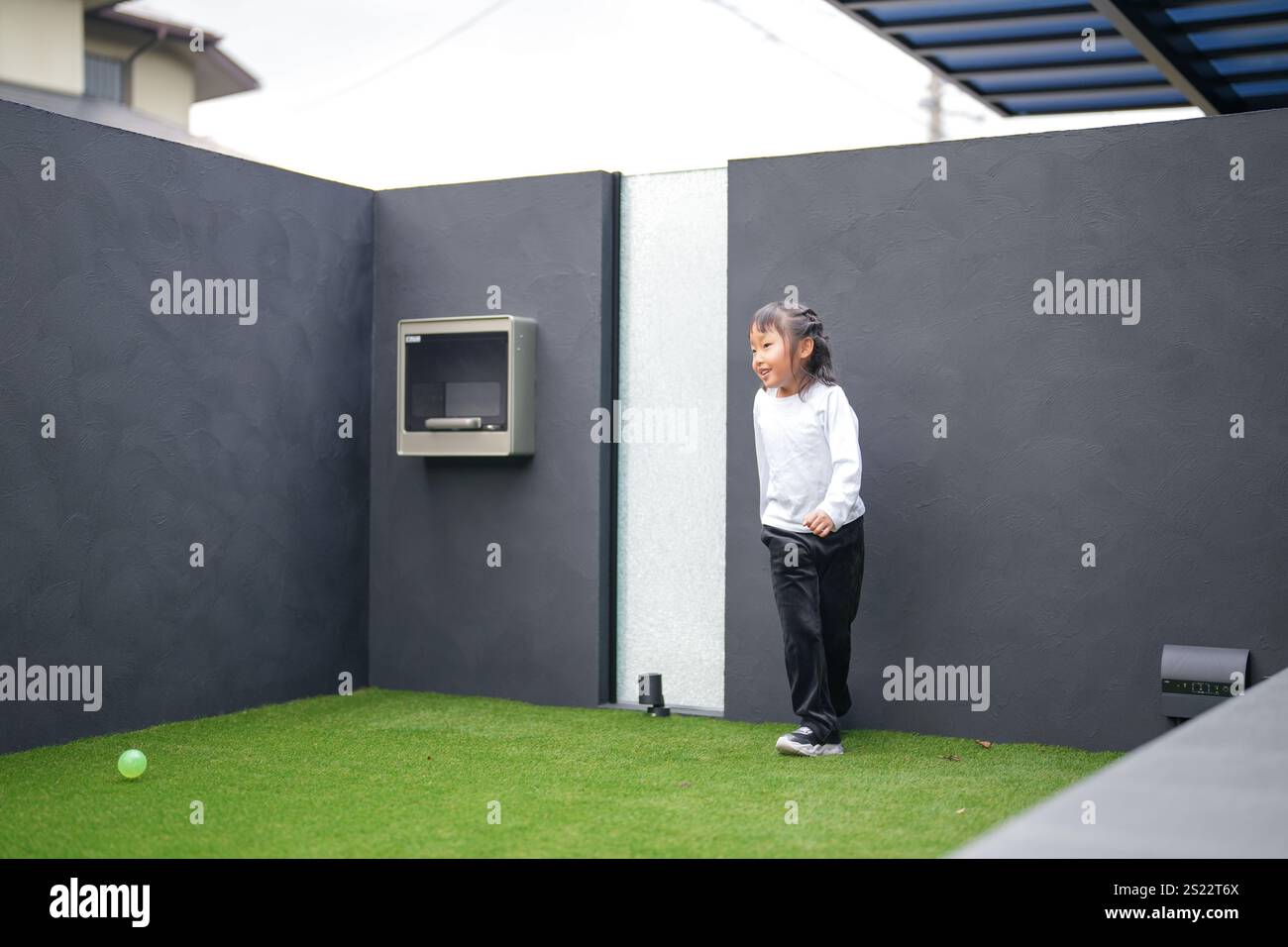 Un parent japonais et un enfant, un homme dans la vingtaine et une fille de 6 ans, jouent en se jetant des balles en plastique vert l'un sur l'autre dans le jardin clôturé de Banque D'Images