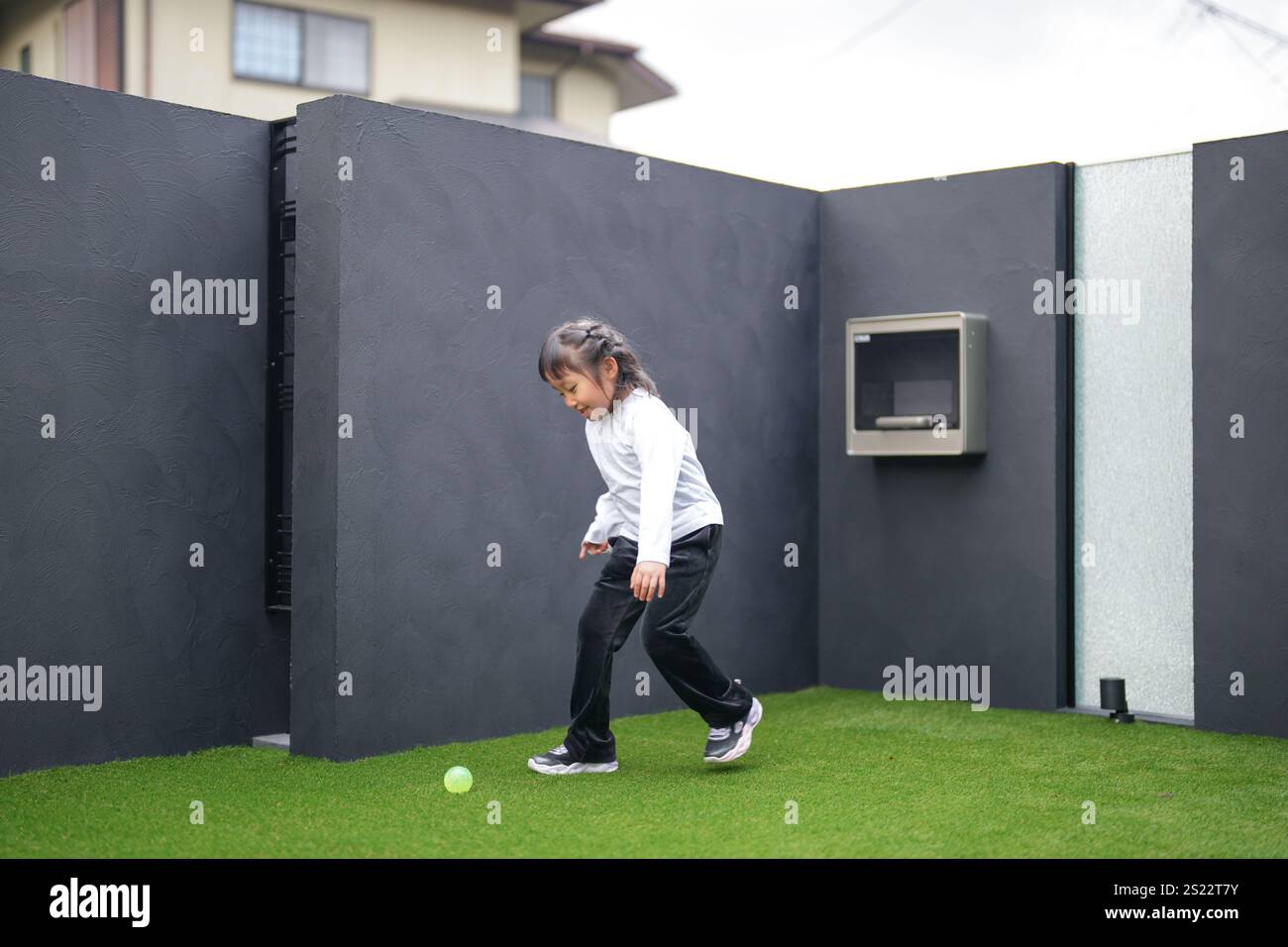 Un parent japonais et un enfant, un homme dans la vingtaine et une fille de 6 ans, jouent en se jetant des balles en plastique vert l'un sur l'autre dans le jardin clôturé de Banque D'Images