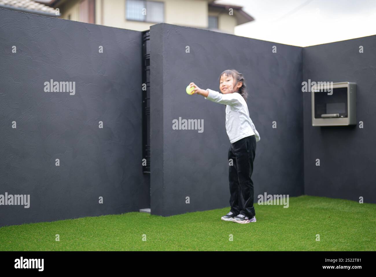 Un parent japonais et un enfant, un homme dans la vingtaine et une fille de 6 ans, jouent en se jetant des balles en plastique vert l'un sur l'autre dans le jardin clôturé de Banque D'Images