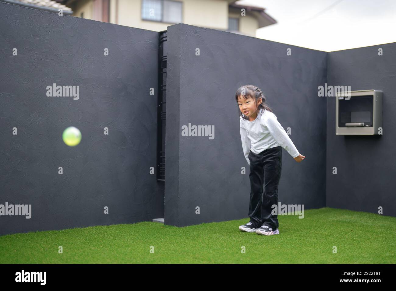 Un parent japonais et un enfant, un homme dans la vingtaine et une fille de 6 ans, jouent en se jetant des balles en plastique vert l'un sur l'autre dans le jardin clôturé de Banque D'Images
