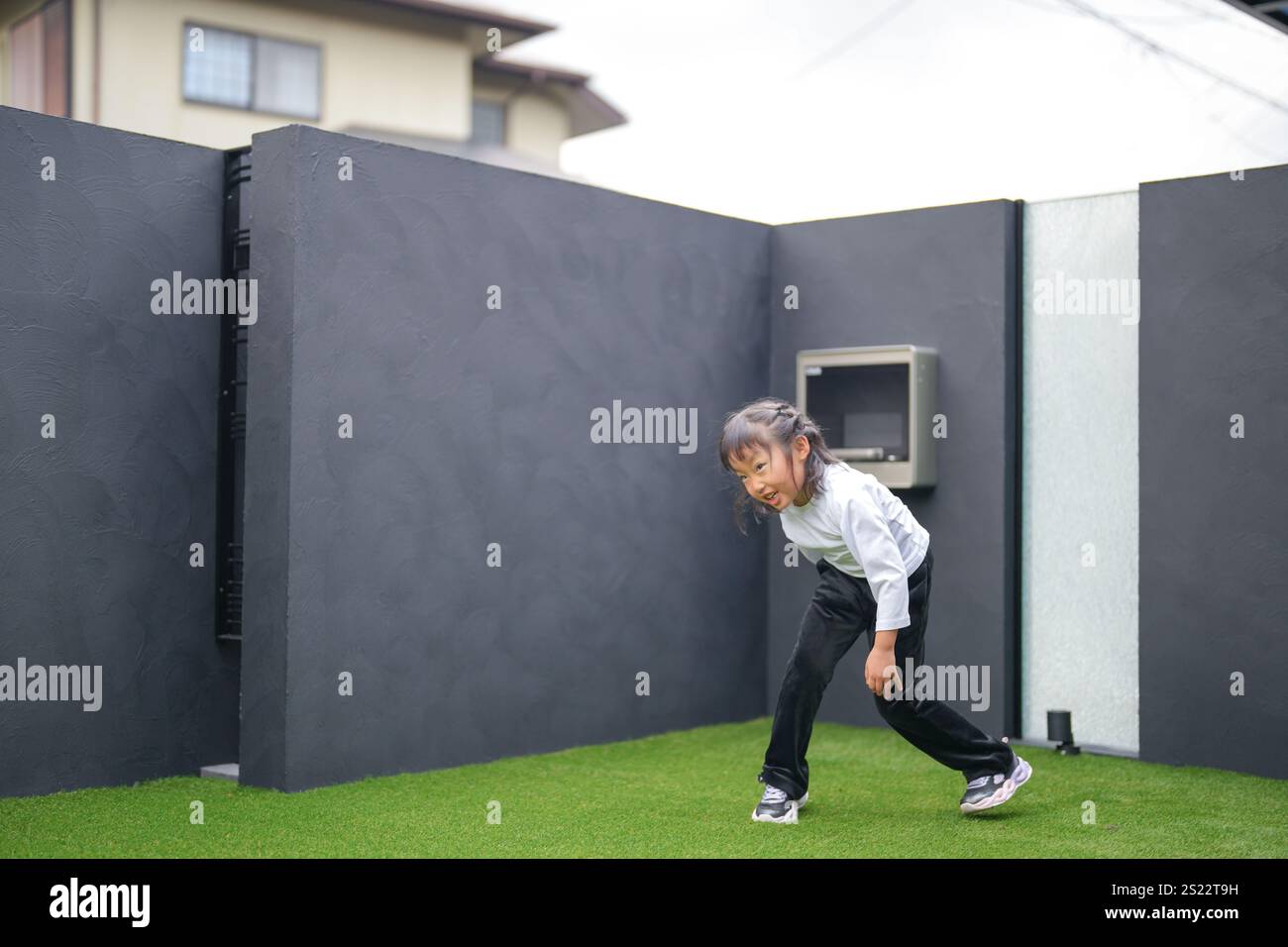 Un parent japonais et un enfant, un homme dans la vingtaine et une fille de 6 ans, jouent en se jetant des balles en plastique vert l'un sur l'autre dans le jardin clôturé de Banque D'Images