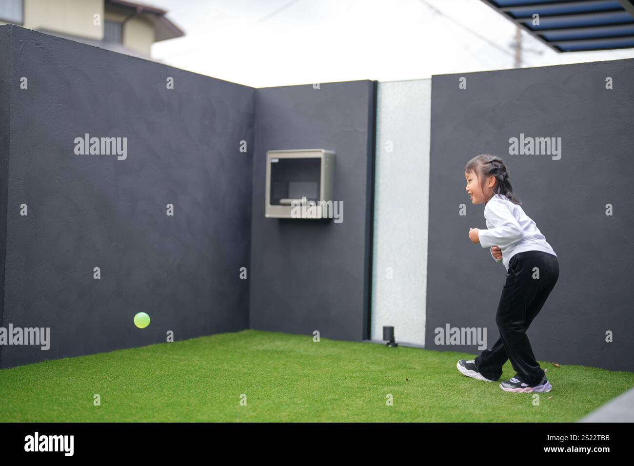 Un parent japonais et un enfant, un homme dans la vingtaine et une fille de 6 ans, jouent en se jetant des balles en plastique vert l'un sur l'autre dans le jardin clôturé de Banque D'Images