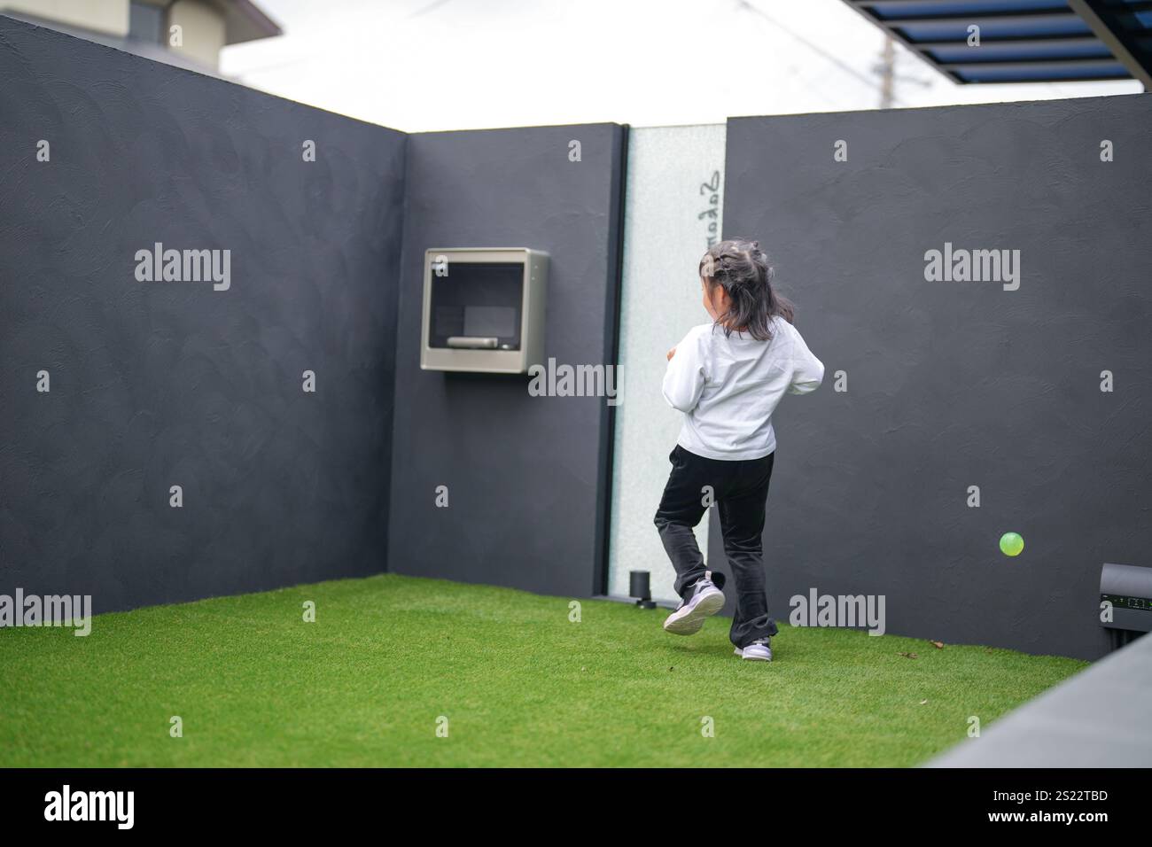 Un parent japonais et un enfant, un homme dans la vingtaine et une fille de 6 ans, jouent en se jetant des balles en plastique vert l'un sur l'autre dans le jardin clôturé de Banque D'Images