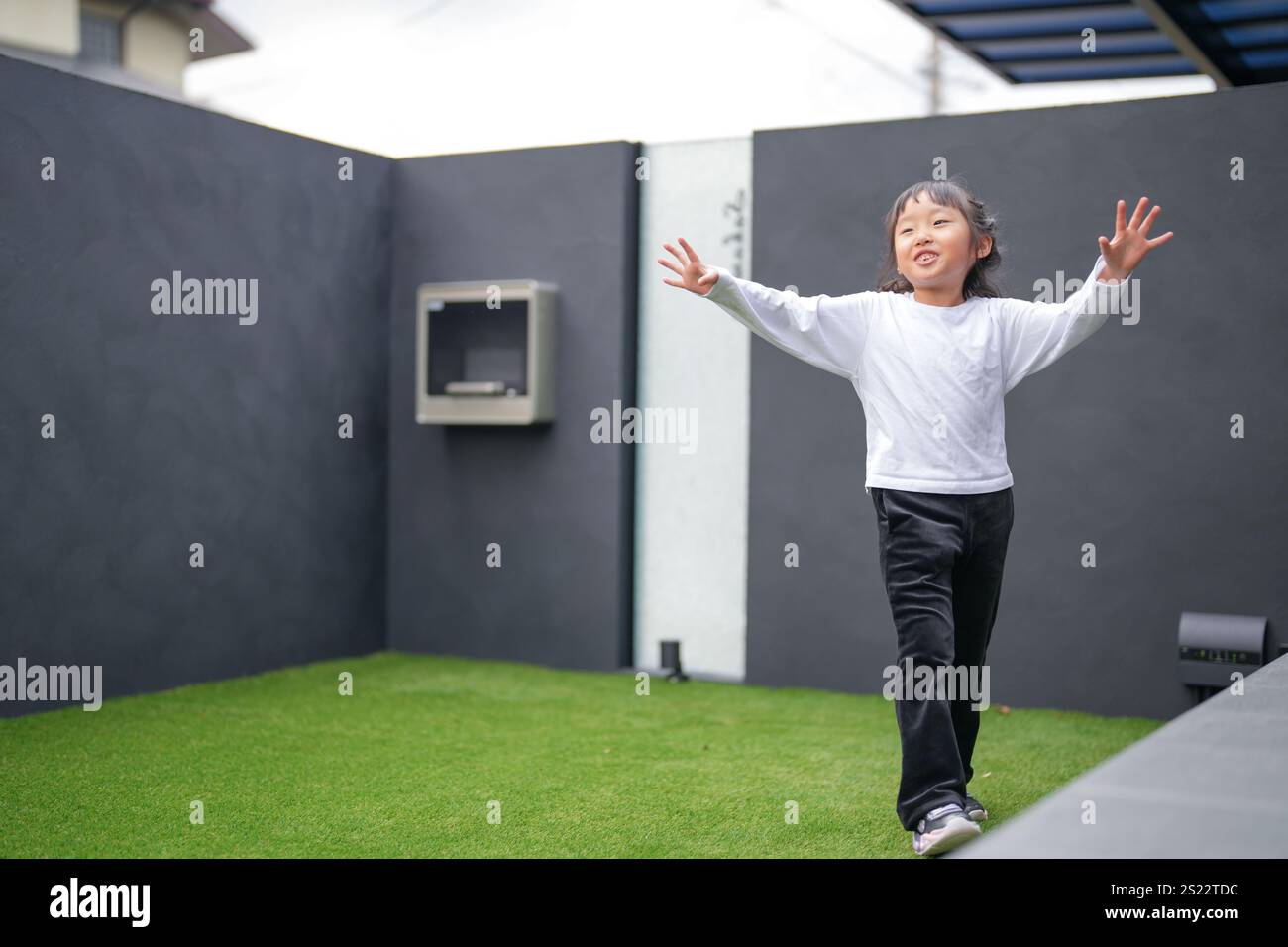 Un parent japonais et un enfant, un homme dans la vingtaine et une fille de 6 ans, jouent en se jetant des balles en plastique vert l'un sur l'autre dans le jardin clôturé de Banque D'Images