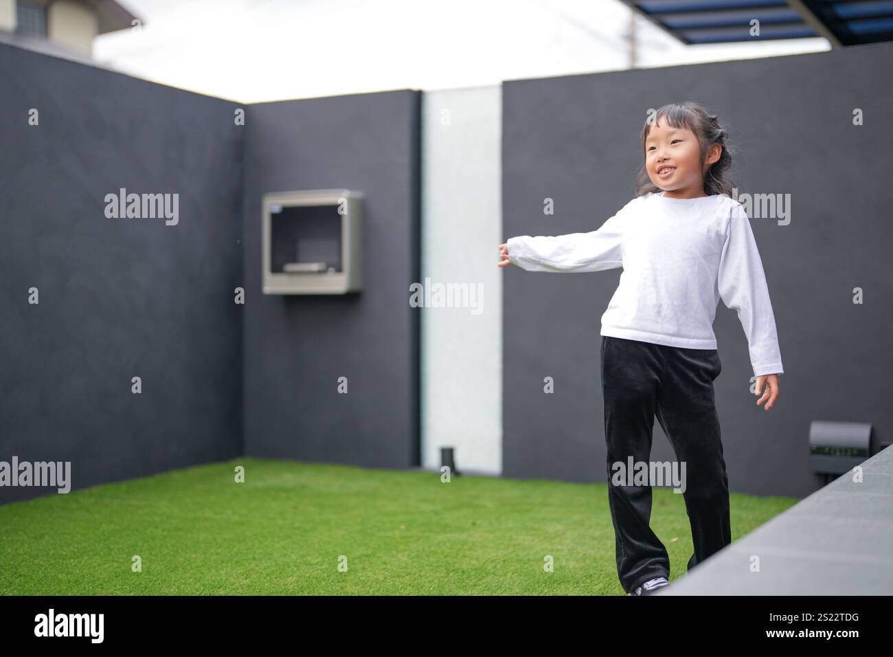 Un parent japonais et un enfant, un homme dans la vingtaine et une fille de 6 ans, jouent en se jetant des balles en plastique vert l'un sur l'autre dans le jardin clôturé de Banque D'Images