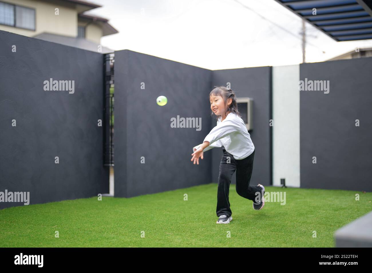 Un parent japonais et un enfant, un homme dans la vingtaine et une fille de 6 ans, jouent en se jetant des balles en plastique vert l'un sur l'autre dans le jardin clôturé de Banque D'Images