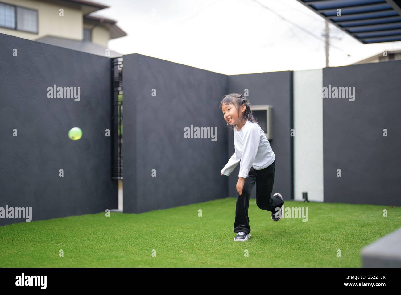 Un parent japonais et un enfant, un homme dans la vingtaine et une fille de 6 ans, jouent en se jetant des balles en plastique vert l'un sur l'autre dans le jardin clôturé de Banque D'Images
