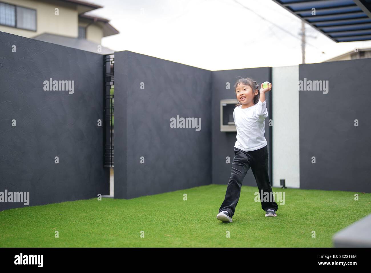 Un parent japonais et un enfant, un homme dans la vingtaine et une fille de 6 ans, jouent en se jetant des balles en plastique vert l'un sur l'autre dans le jardin clôturé de Banque D'Images