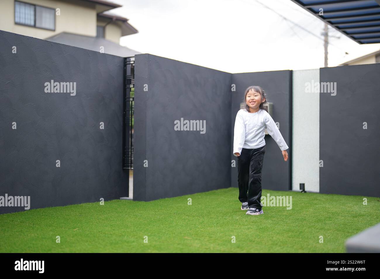 Un parent japonais et un enfant, un homme dans la vingtaine et une fille de 6 ans, jouent en se jetant des balles en plastique vert l'un sur l'autre dans le jardin clôturé de Banque D'Images