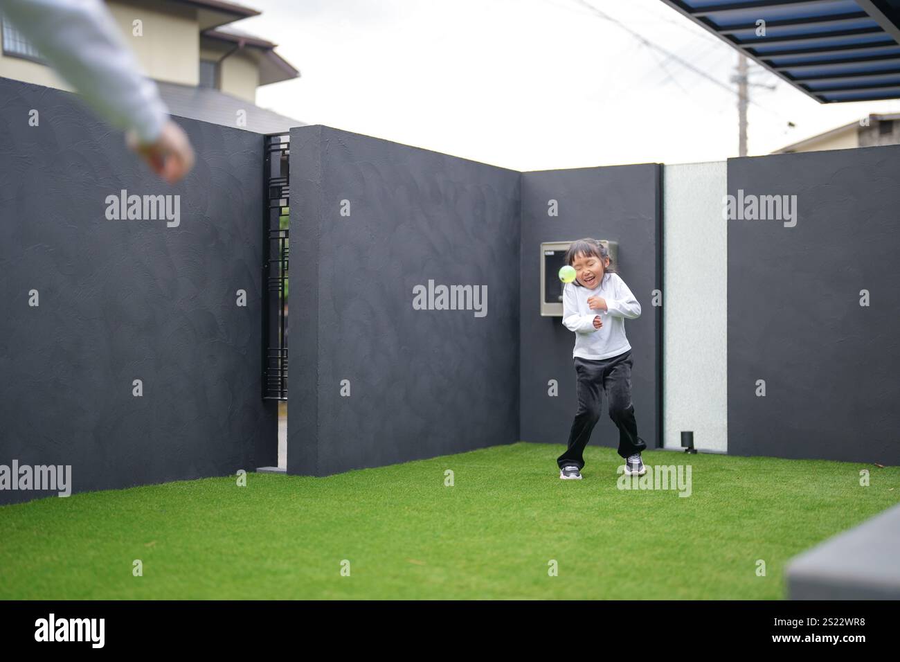 Un parent japonais et un enfant, un homme dans la vingtaine et une fille de 6 ans, jouent en se jetant des balles en plastique vert l'un sur l'autre dans le jardin clôturé de Banque D'Images