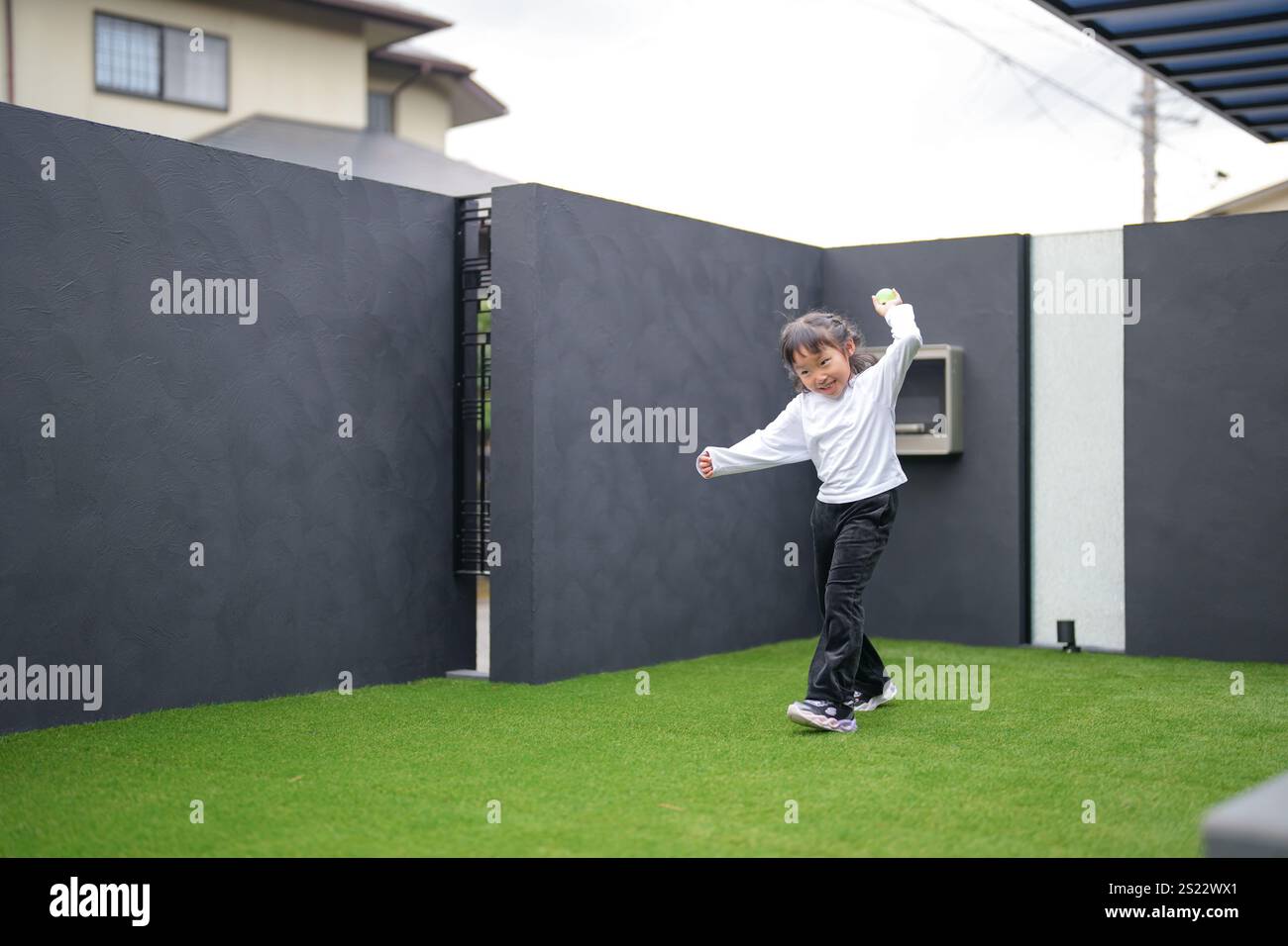 Un parent japonais et un enfant, un homme dans la vingtaine et une fille de 6 ans, jouent en se jetant des balles en plastique vert l'un sur l'autre dans le jardin clôturé de Banque D'Images