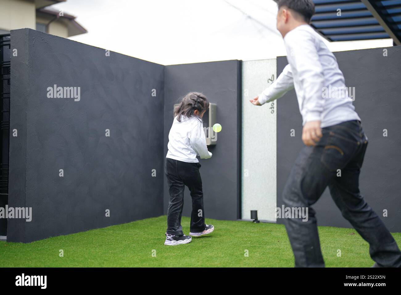 Un parent japonais et un enfant, un homme dans la vingtaine et une fille de 6 ans, jouent en se jetant des balles en plastique vert l'un sur l'autre dans le jardin clôturé de Banque D'Images