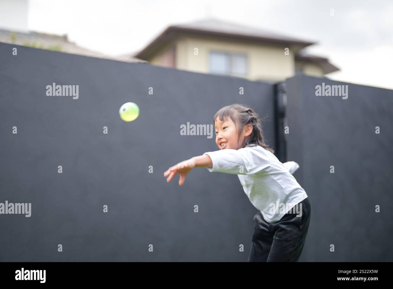 Un parent japonais et un enfant, un homme dans la vingtaine et une fille de 6 ans, jouent en se jetant des balles en plastique vert l'un sur l'autre dans le jardin clôturé de Banque D'Images