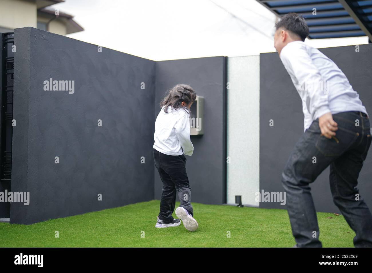 Un parent japonais et un enfant, un homme dans la vingtaine et une fille de 6 ans, jouent en se jetant des balles en plastique vert l'un sur l'autre dans le jardin clôturé de Banque D'Images