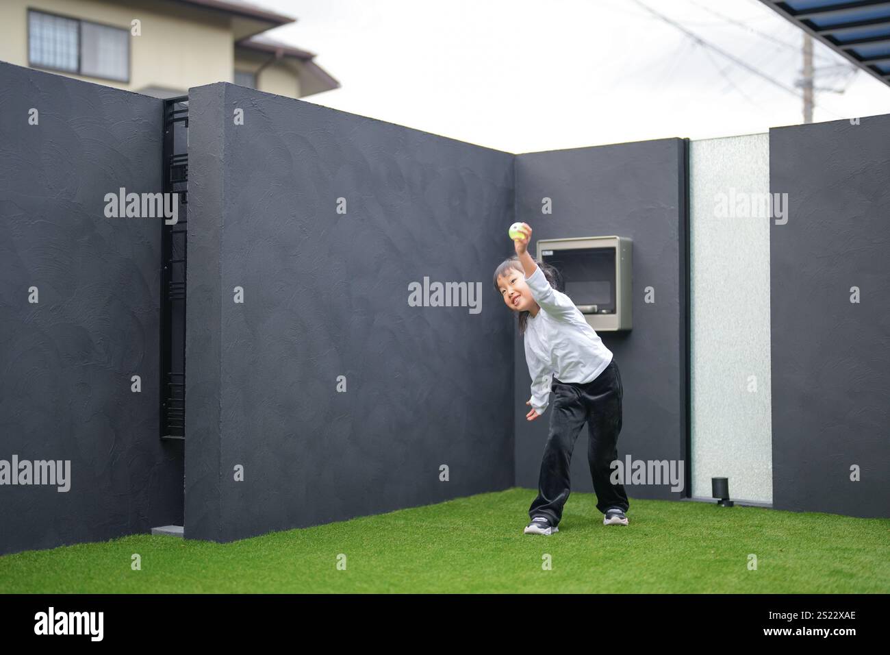 Un parent japonais et un enfant, un homme dans la vingtaine et une fille de 6 ans, jouent en se jetant des balles en plastique vert l'un sur l'autre dans le jardin clôturé de Banque D'Images