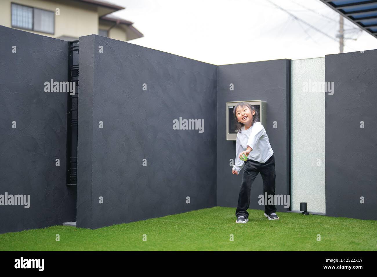 Un parent japonais et un enfant, un homme dans la vingtaine et une fille de 6 ans, jouent en se jetant des balles en plastique vert l'un sur l'autre dans le jardin clôturé de Banque D'Images