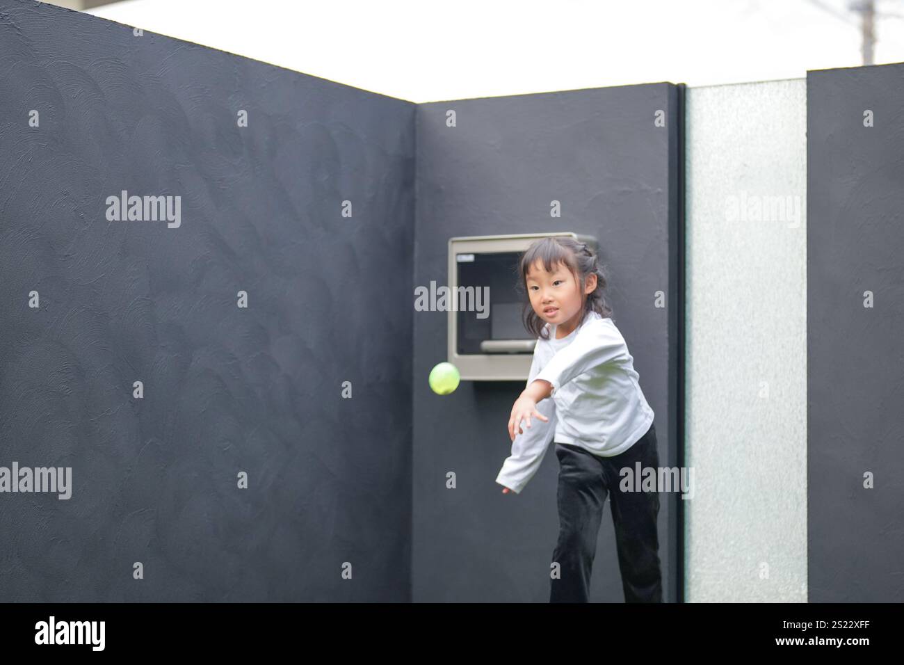 Un parent japonais et un enfant, un homme dans la vingtaine et une fille de 6 ans, jouent en se jetant des balles en plastique vert l'un sur l'autre dans le jardin clôturé de Banque D'Images