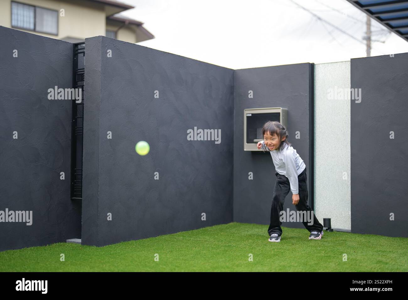 Un parent japonais et un enfant, un homme dans la vingtaine et une fille de 6 ans, jouent en se jetant des balles en plastique vert l'un sur l'autre dans le jardin clôturé de Banque D'Images