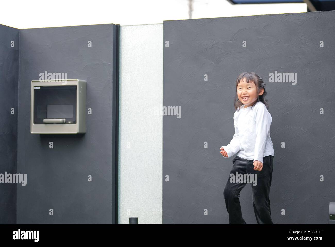 Un parent japonais et un enfant, un homme dans la vingtaine et une fille de 6 ans, jouent en se jetant des balles en plastique vert l'un sur l'autre dans le jardin clôturé de Banque D'Images