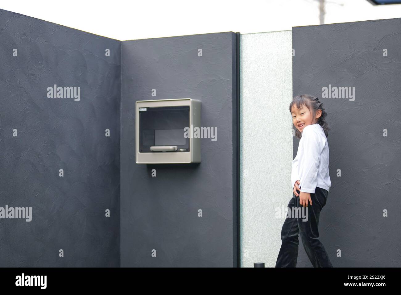 Un parent japonais et un enfant, un homme dans la vingtaine et une fille de 6 ans, jouent en se jetant des balles en plastique vert l'un sur l'autre dans le jardin clôturé de Banque D'Images