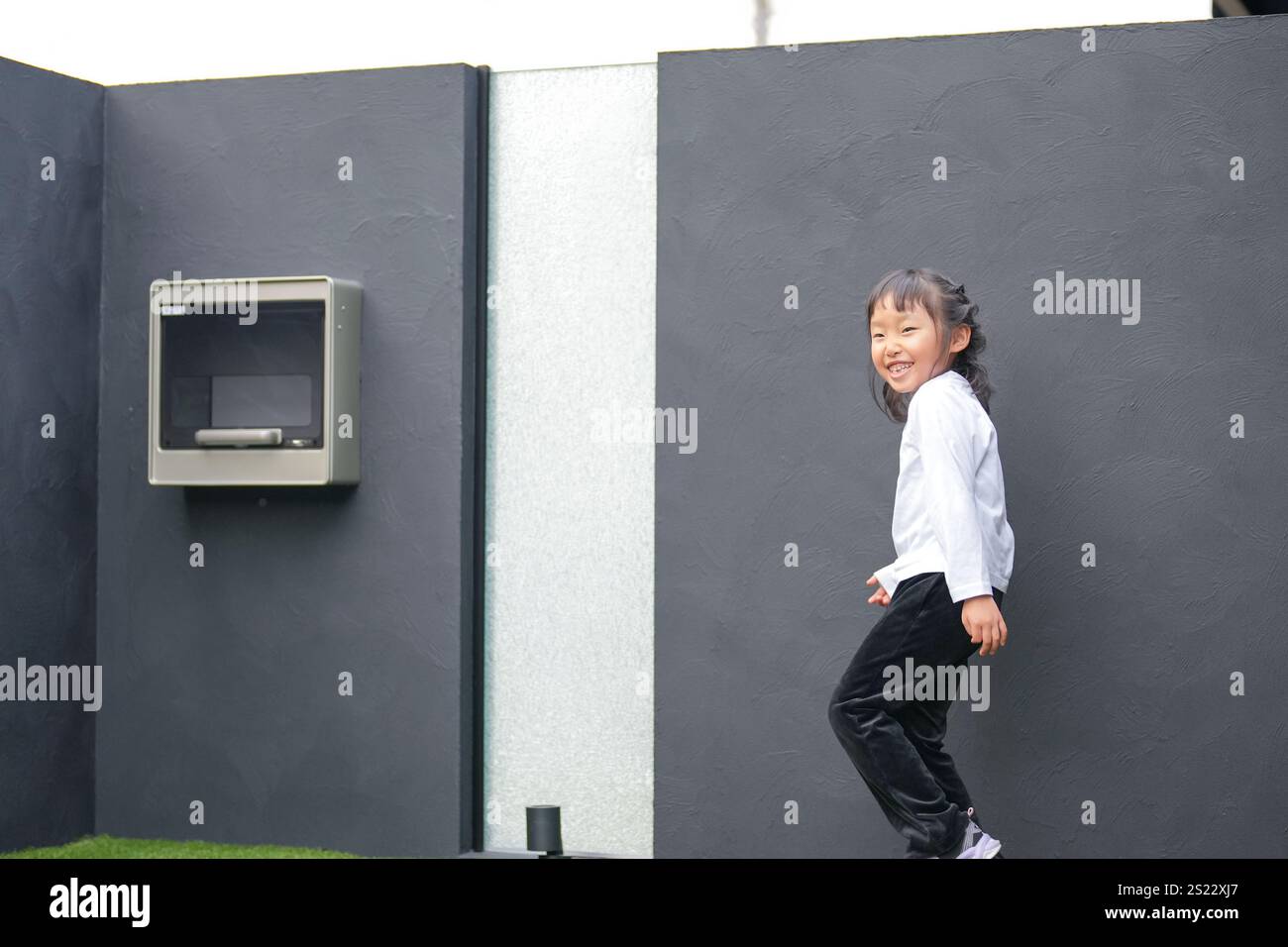 Un parent japonais et un enfant, un homme dans la vingtaine et une fille de 6 ans, jouent en se jetant des balles en plastique vert l'un sur l'autre dans le jardin clôturé de Banque D'Images