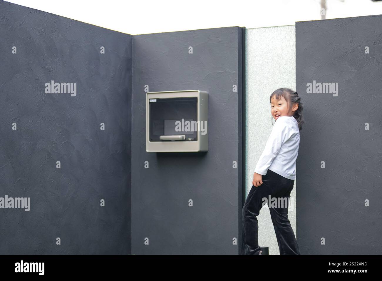 Un parent japonais et un enfant, un homme dans la vingtaine et une fille de 6 ans, jouent en se jetant des balles en plastique vert l'un sur l'autre dans le jardin clôturé de Banque D'Images
