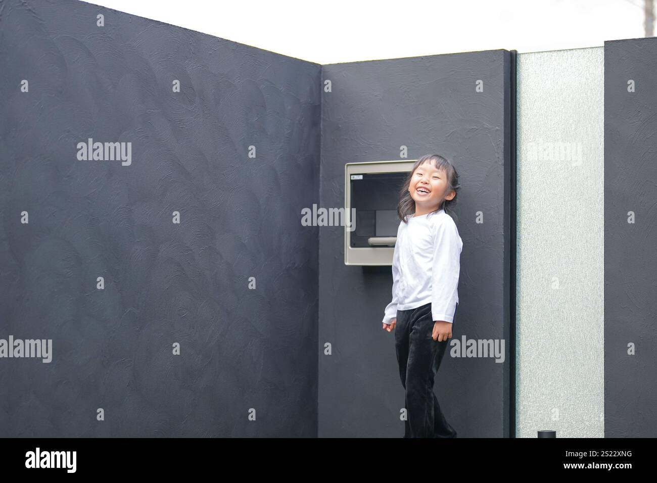 Un parent japonais et un enfant, un homme dans la vingtaine et une fille de 6 ans, jouent en se jetant des balles en plastique vert l'un sur l'autre dans le jardin clôturé de Banque D'Images