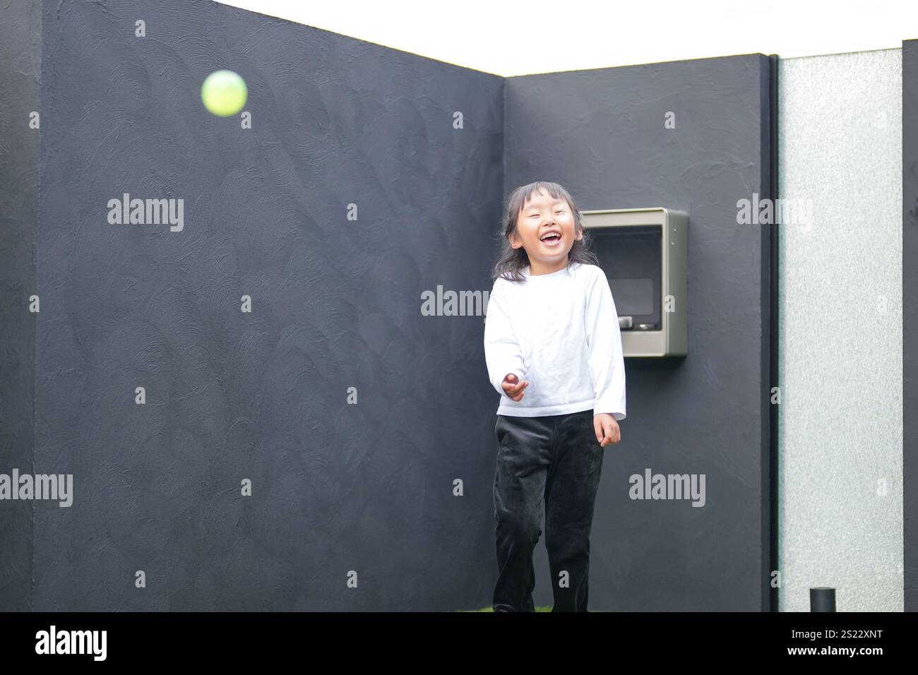Un parent japonais et un enfant, un homme dans la vingtaine et une fille de 6 ans, jouent en se jetant des balles en plastique vert l'un sur l'autre dans le jardin clôturé de Banque D'Images