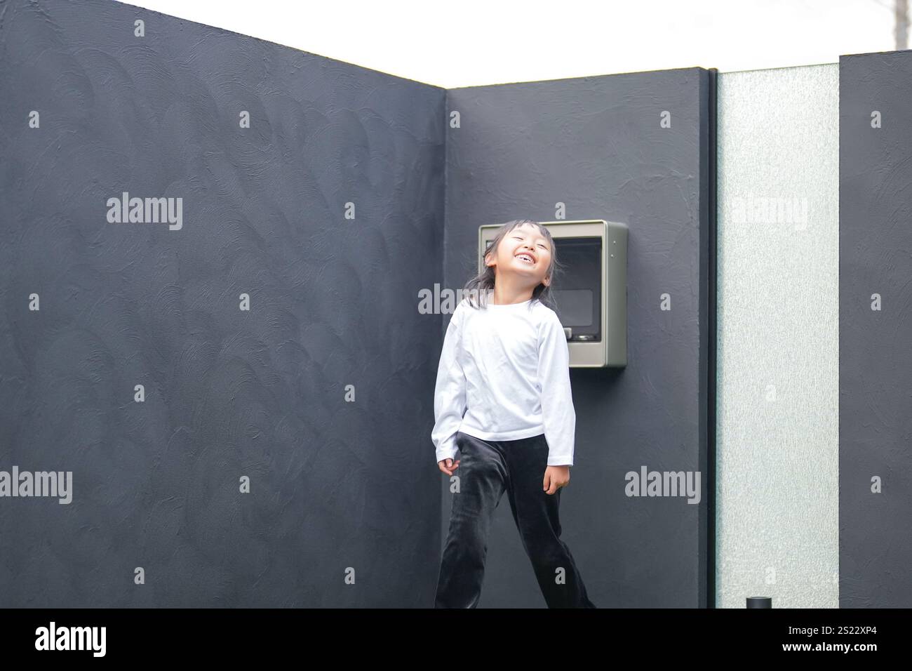 Un parent japonais et un enfant, un homme dans la vingtaine et une fille de 6 ans, jouent en se jetant des balles en plastique vert l'un sur l'autre dans le jardin clôturé de Banque D'Images