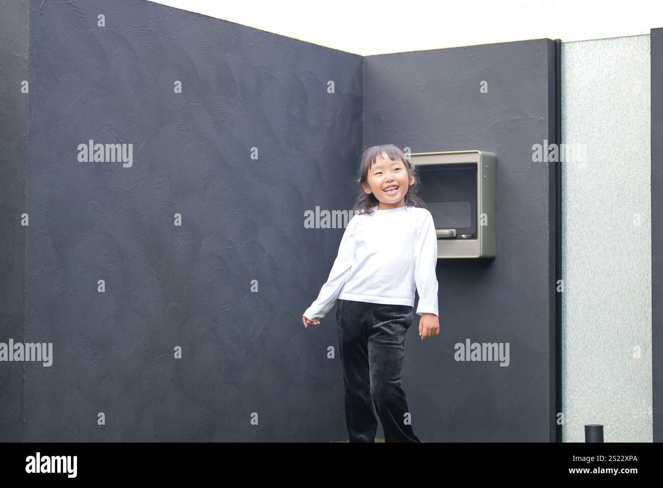 Un parent japonais et un enfant, un homme dans la vingtaine et une fille de 6 ans, jouent en se jetant des balles en plastique vert l'un sur l'autre dans le jardin clôturé de Banque D'Images