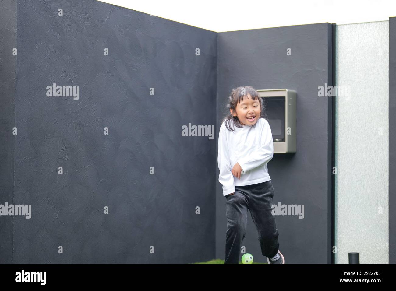 Un parent japonais et un enfant, un homme dans la vingtaine et une fille de 6 ans, jouent en se jetant des balles en plastique vert l'un sur l'autre dans le jardin clôturé de Banque D'Images