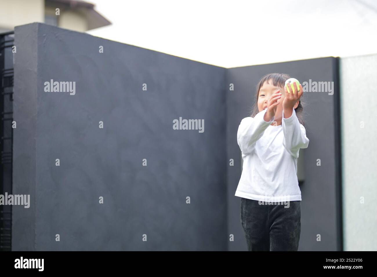 Un parent japonais et un enfant, un homme dans la vingtaine et une fille de 6 ans, jouent en se jetant des balles en plastique vert l'un sur l'autre dans le jardin clôturé de Banque D'Images