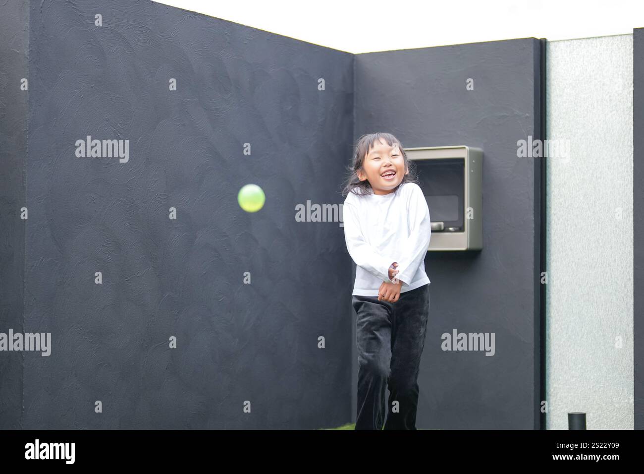 Un parent japonais et un enfant, un homme dans la vingtaine et une fille de 6 ans, jouent en se jetant des balles en plastique vert l'un sur l'autre dans le jardin clôturé de Banque D'Images