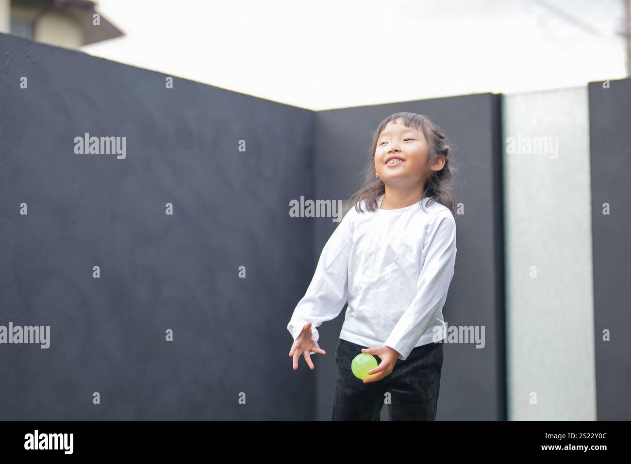 Un parent japonais et un enfant, un homme dans la vingtaine et une fille de 6 ans, jouent en se jetant des balles en plastique vert l'un sur l'autre dans le jardin clôturé de Banque D'Images