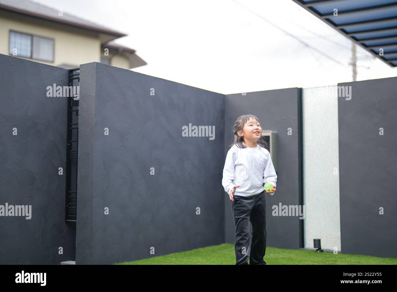 Un parent japonais et un enfant, un homme dans la vingtaine et une fille de 6 ans, jouent en se jetant des balles en plastique vert l'un sur l'autre dans le jardin clôturé de Banque D'Images
