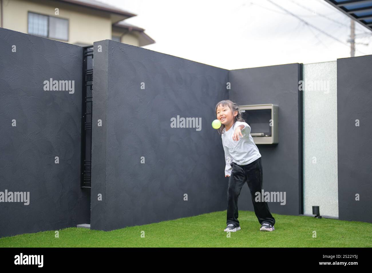 Un parent japonais et un enfant, un homme dans la vingtaine et une fille de 6 ans, jouent en se jetant des balles en plastique vert l'un sur l'autre dans le jardin clôturé de Banque D'Images